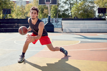 Image of athlete man in blue T-shirt playing basketball on playground.