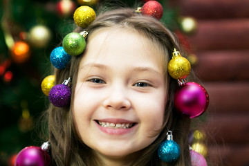 Fototapeta na wymiar Merry girl on new years eve Little girl with a garland and Christmas balls in her hair on her head laughing before Christmas