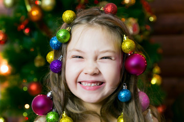 Fototapeta na wymiar Merry girl on new years eve Little girl with a garland Christmas balls in her hair on her head laughing before Christmas