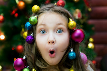 Little girl with garland and Christmas balls in her hair on her head laughing before Christmas