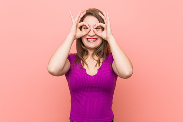 Young hispanic woman against a pink wall showing okay sign over eyes