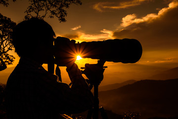 Silhouette of a landscape photographer use super telephoto lens at top of mountains during sunset sky