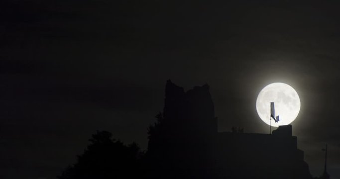 4k night time lapse of full moon rising from behind castle ruins