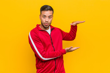 Young filipino fitness man shocked and amazed holding a copy space between hands.