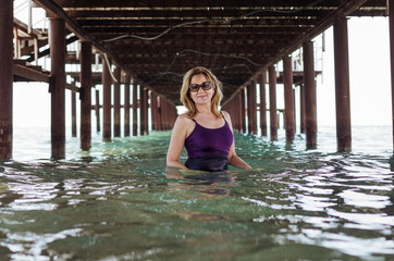 A pretty elderly blonde woman smiling happily as she stands under the bridge in the water