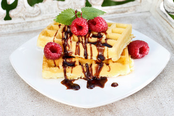 Waffles with chocolate raspberries on wooden table.