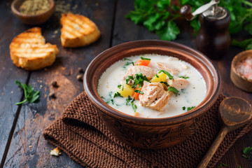 Warm Finnish creamy soup with salmon and vegetables in old ceramic bowl on old wooden background. Rustic style.