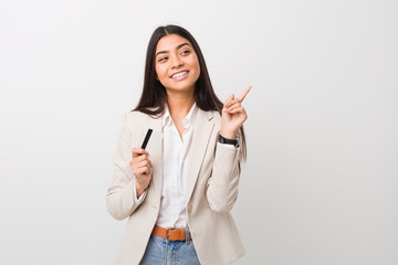 Young arab woman holding a credit card smiling cheerfully pointing with forefinger away.