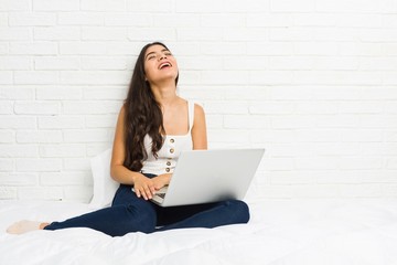 Young arab woman working with her laptop on the bed relaxed and happy laughing, neck stretched showing teeth.