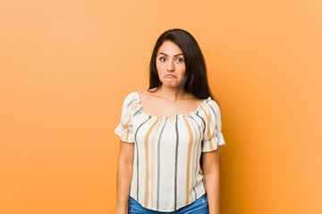 Obraz premium Young curvy woman shrugs shoulders and open eyes confused.