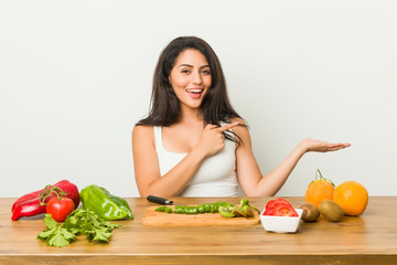 Young curvy woman preparing a healthy meal excited holding a copy space on palm.