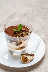 Portion of Classic tiramisu dessert in a glass cup on concrete background
