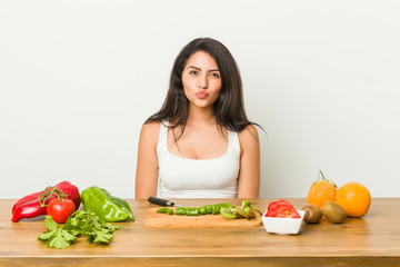 Young curvy woman preparing a healthy meal blows cheeks, has tired expression. Facial expression concept.