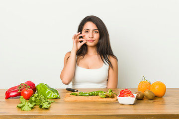 Young curvy woman preparing a healthy meal with fingers on lips keeping a secret.