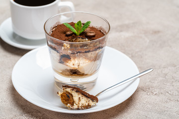 Portion of Classic tiramisu dessert in a glass and cup of coffee on concrete background