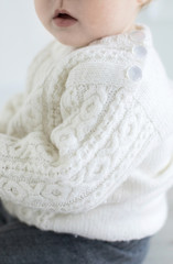 Young children dressed in woolen clothes in a cozy Scandinavian environment play with wooden toys against a white wall of a room.