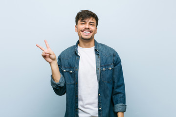 Young hispanic cool man joyful and carefree showing a peace symbol with fingers.