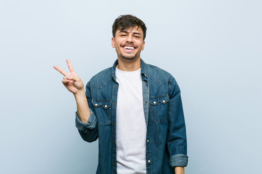 Young hispanic cool man joyful and carefree showing a peace symbol with fingers.