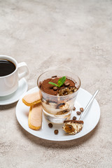 Portion of Classic tiramisu dessert in a glass, savoiardi cookies and cup of coffee on concrete background