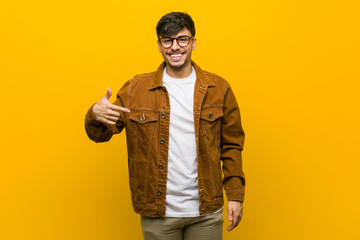 Young hispanic casual man person pointing by hand to a shirt copy space, proud and confident