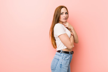 Young redhead ginger woman against a pink wall scared and afraid.