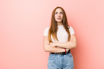 Young redhead ginger woman against a pink wall tired of a repetitive task.