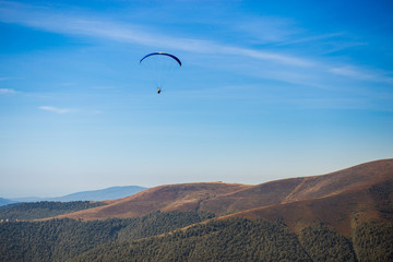 Fototapeta na wymiar Paraglider flying over mountains peak in autumn day with beautiful aerial world view. Freedom lifestyle concept