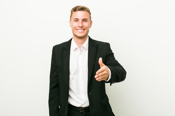 Young caucasian business man stretching hand at camera in greeting gesture.