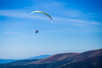 Paraglide silhouette flying over Carpathian peaks mountains on blue sky background. Feeling of freedom