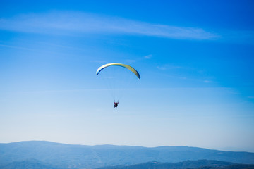 Paraglide silhouette flying over Carpathian peaks mountains on blue sky background. Feeling of freedom
