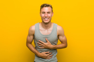 Young caucasian sport man laughs happily and has fun keeping hands on stomach.