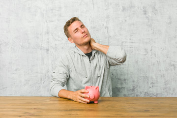 Fototapeta premium Young man saving money with a piggy bank suffering neck pain due to sedentary lifestyle.