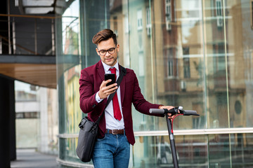 Young businessman with electric scooter standing in front of modern business building looking at phone. © Zoran Zeremski