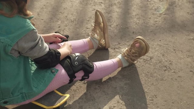 Little girl dresses protection: helmet, knee pads and elbow pads. Sunset
