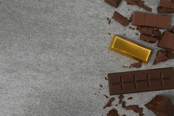 Broken chocolate with small piece and gold on tile table.