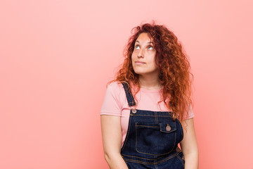 Young pretty ginger redhead woman wearing a jeans dungaree dreaming of achieving goals and purposes