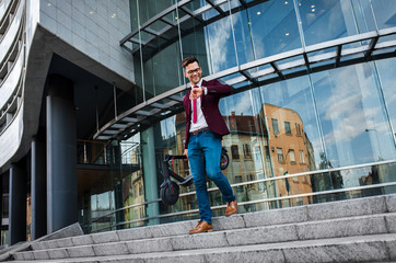 Young businessman with electric scooter standing in front of modern business building looking at watch.