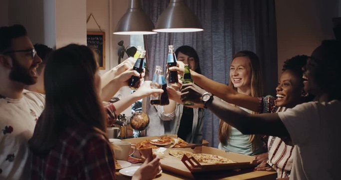 Young cheerful multiethnic friends having pizza and drinks, raise a toast together at celebration party slow motion.