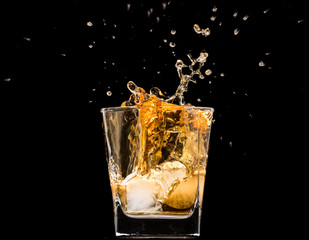 glass of whiskey with ice and a splash and spray from falling on a black background