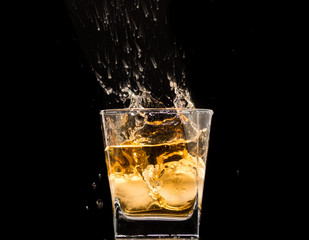 Fototapeta na wymiar glass of whiskey with ice and a splash and spray from falling on a black background