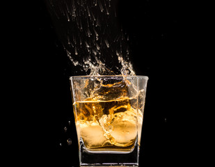 glass of whiskey with ice and a splash and spray from falling on a black background