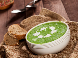 Delicious creamy green vegetable soup with bread close-up on a dark background.
