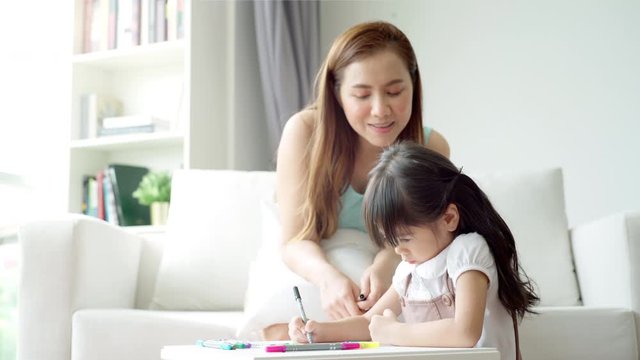 A single mother of  Asian ethnic teaching her daughter to draw at home on a beautiful morning sunshine through the large living room window