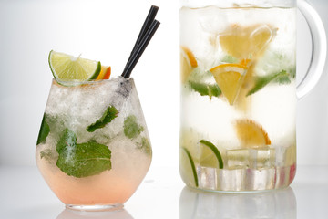 Glass and pitcher of lemonade with lemon, lime and mint on white background.  Soda water with citrus and ice. Lime and orange in sparkling water
