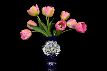 Bouquet of fresh spring tulips in a small blue vase on a contrasting black background