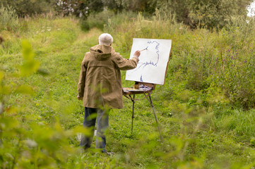 An elderly man is interested in painting with oil paints. Drawing a natural landscape