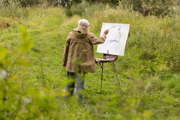 An elderly man is interested in painting with oil paints. Drawing a natural landscape