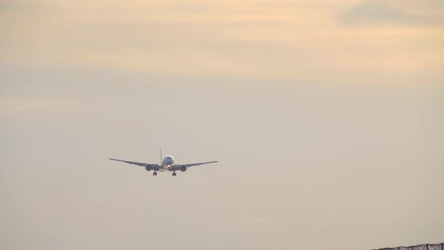 Close up shot of huge commercial jet aircraft silhouette is landing in airport in sunset with wind and yellow clouds
