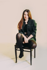 young beautiful fashion model sitting on a retro chair and looking at camera on gray background