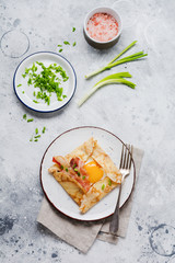 Crepe with fried egg, cheese, bacon and green onions for breakfast on a light gray concrete background.